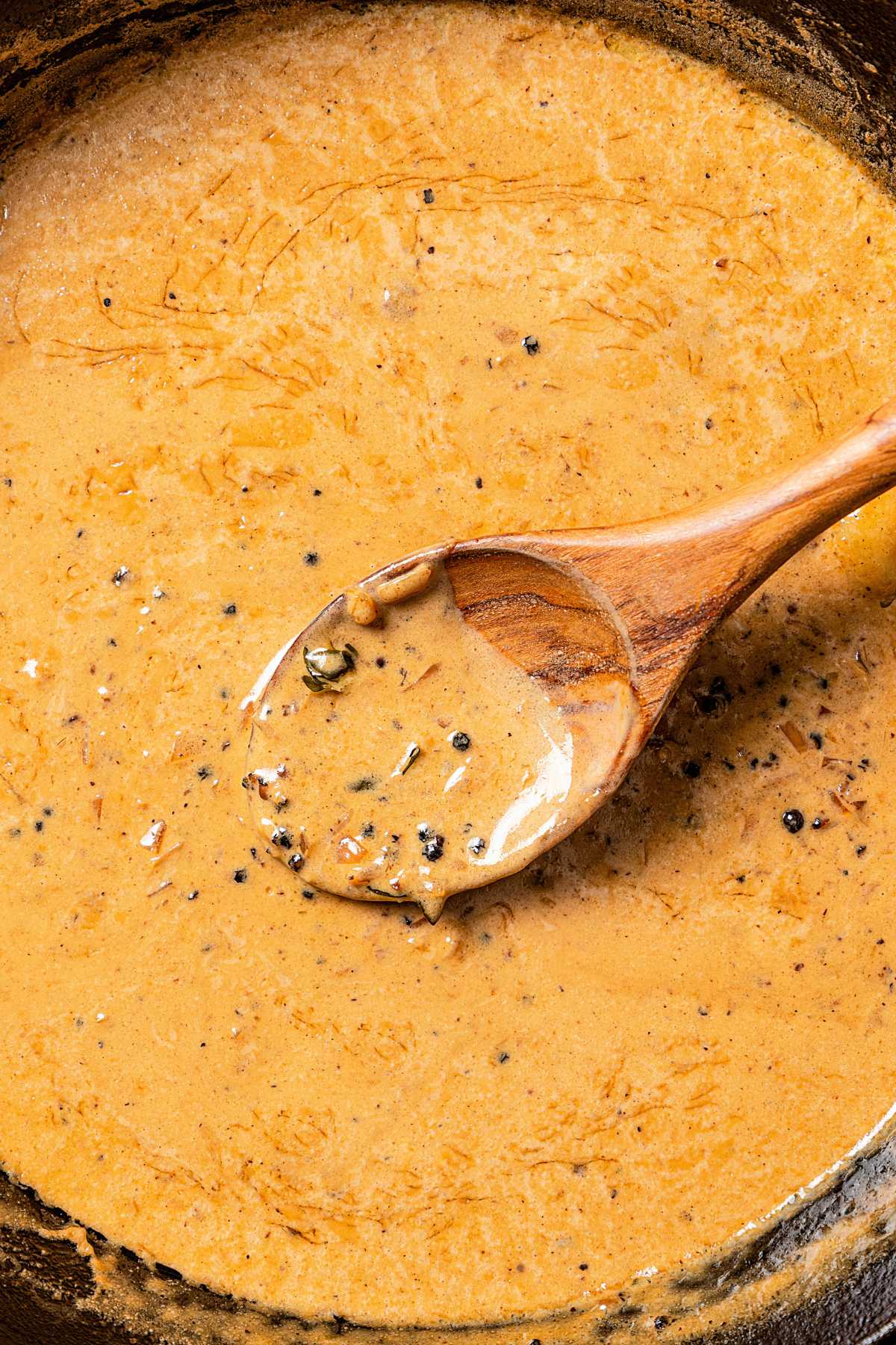 A wooden spoon stirring through au poivre sauce in a skillet.