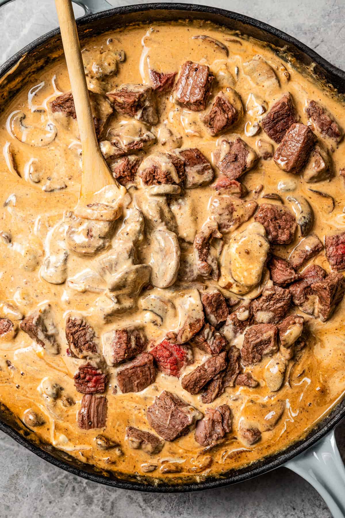 Beef cubes added to mushroom gravy in a skillet.