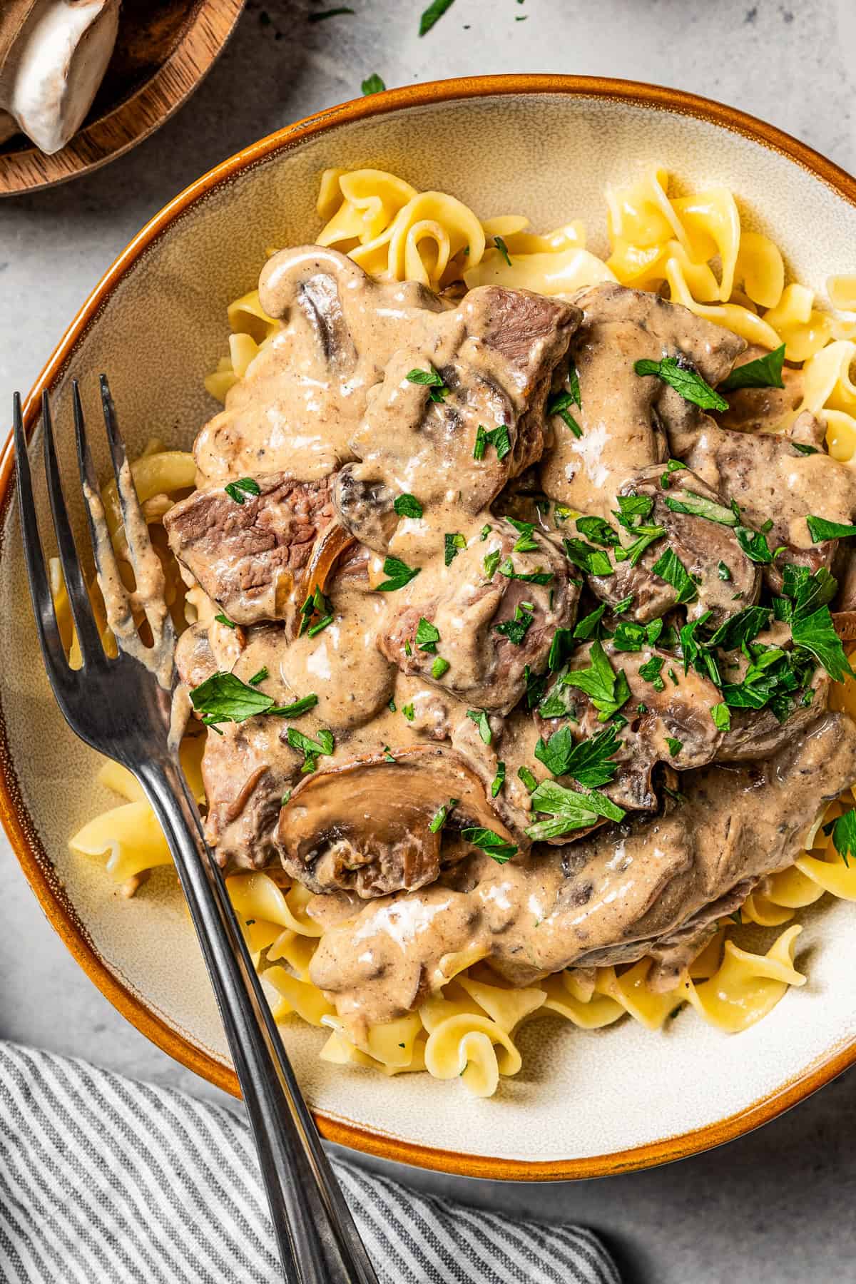 Photo beef stroganoff in a bowl garnished with parsley and a fork in the bowl.