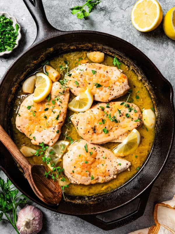 Overhead view of chicken paillard nestled into a large skillet with sauce, garnished with lemon wedges and fresh parsley.