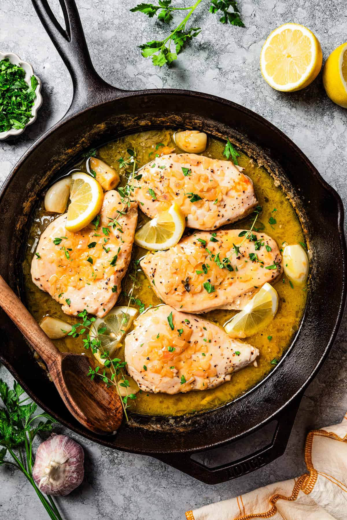 Overhead view of chicken paillard nestled into a large skillet with sauce, garnished with lemon wedges and fresh parsley.