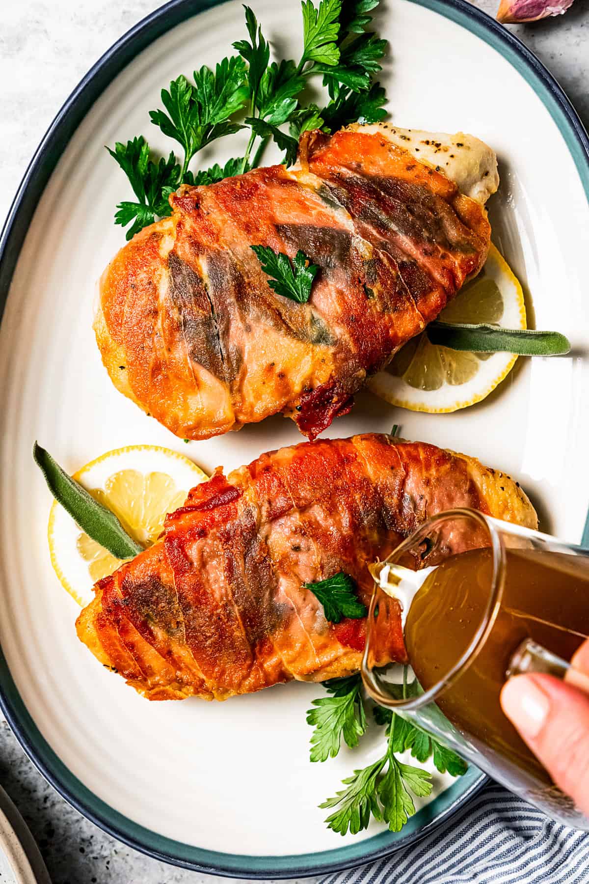 Overhead view of sauce begin poured over chicken saltimbocca on a platter garnished with lemon slices and parsley.