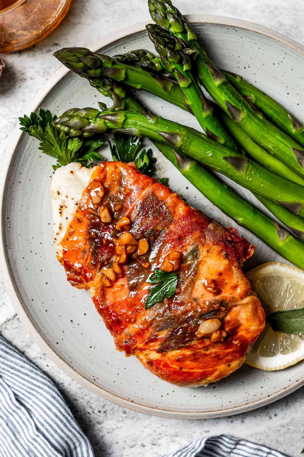 Cooked chicken breast wrapped in prosciutto called chicken saltimbocca and it's served on a dinner plate with a serving of asparagus spears.