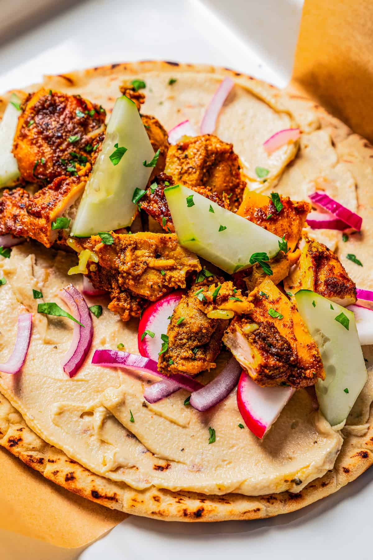 Flatbread spread with hummus and topped with veggies and diced chicken.