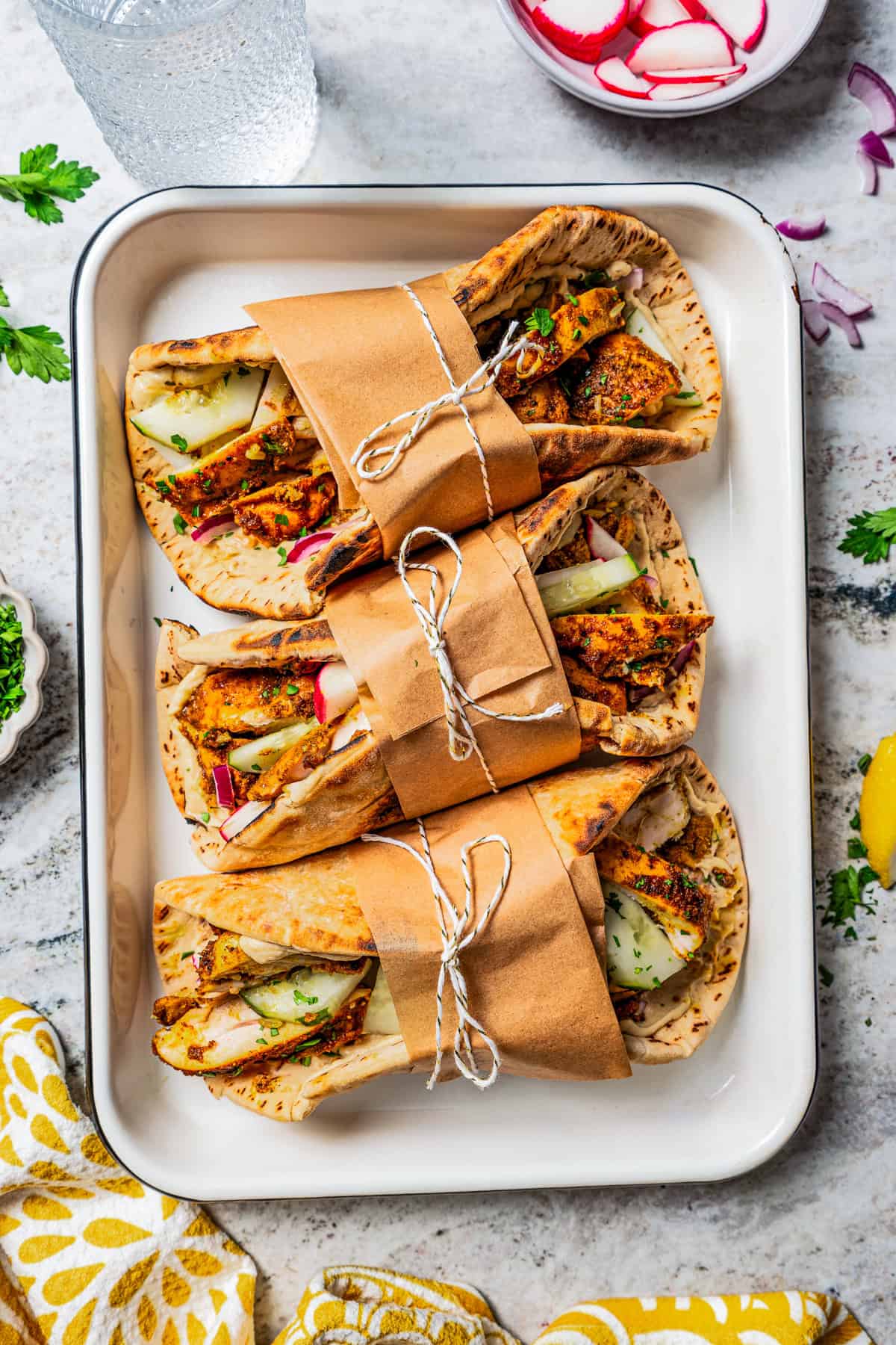 Overhead view of a baking try with three chicken shawarma wraps tied up in paper with string.