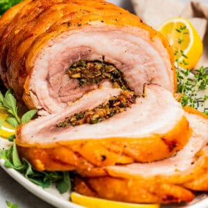 Front view of sliced porchetta on a platter garnished with herbs and lemon slices.