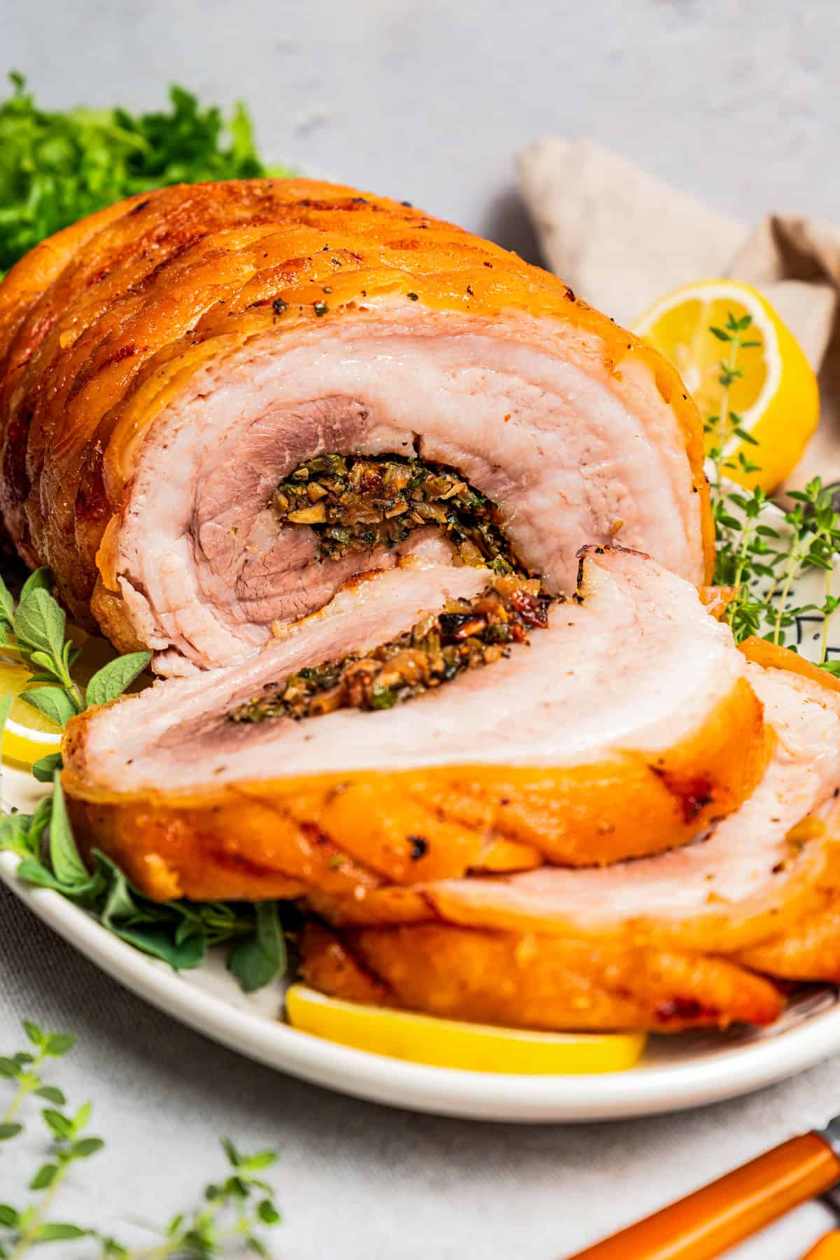 Front view of sliced porchetta on a platter garnished with herbs and lemon slices.