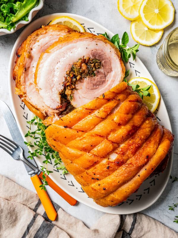 Overhead close up view of sliced porchetta on a platter next to a fork and knife.