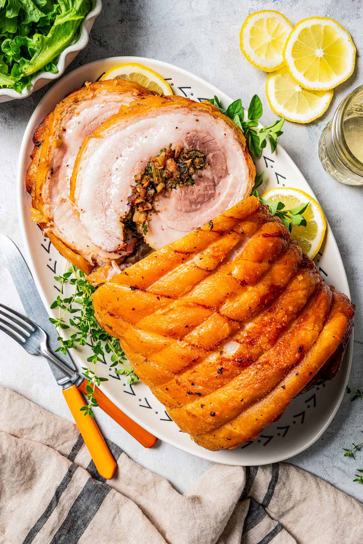 Overhead close up view of sliced porchetta on a platter next to a fork and knife.