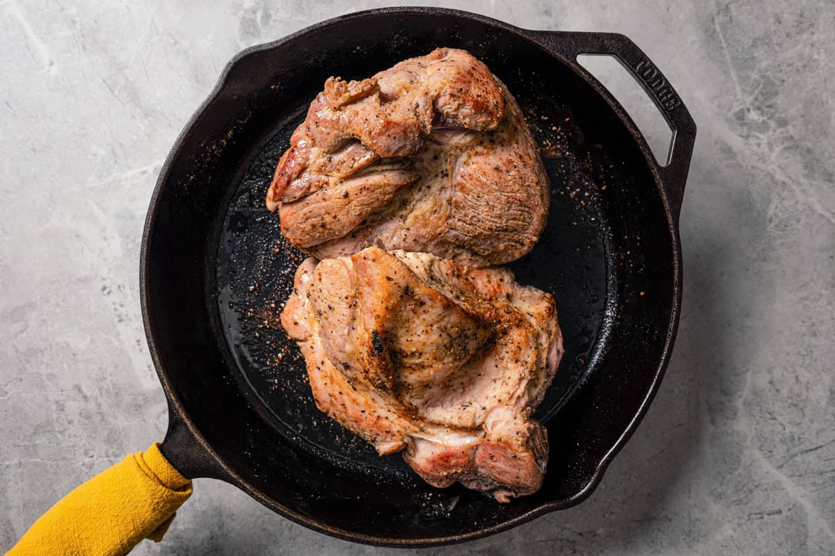 This pork roast recipe is a whole meal in one! With juicy seasoned pork shoulder slow-roasted with fresh citrus, carrots, potatoes, and herbs. Browning a pork shoulder in a skillet.