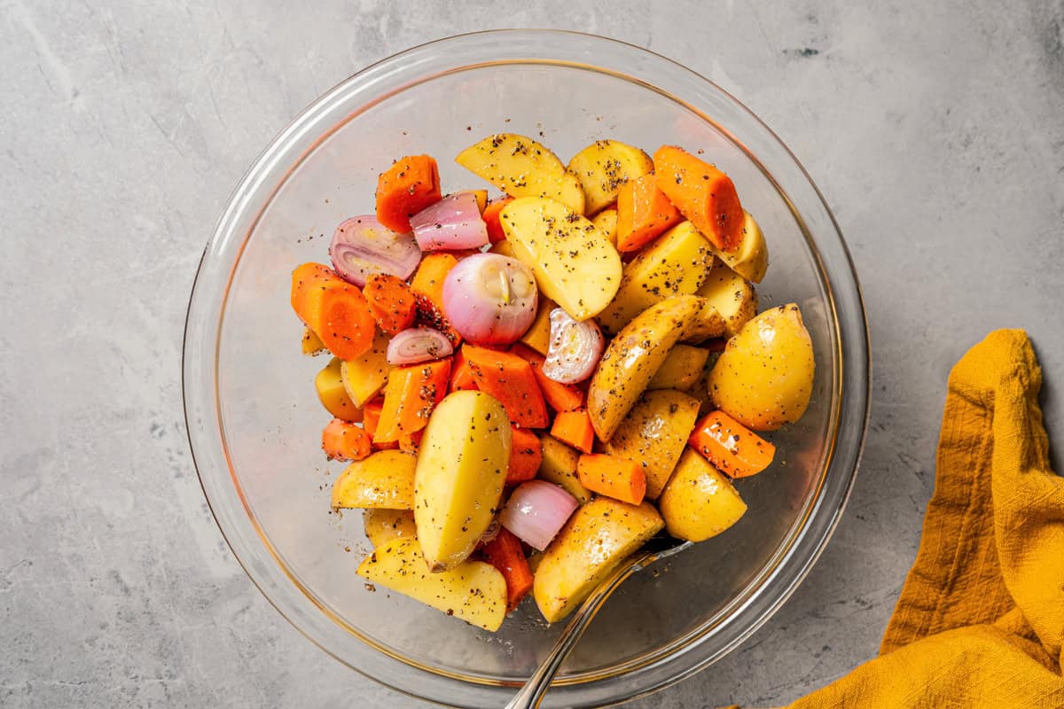 This pork roast recipe is a whole meal in one! With juicy seasoned pork shoulder slow-roasted with fresh citrus, carrots, potatoes, and herbs. A bowl with chopped carrots, potatoes, and shallots.