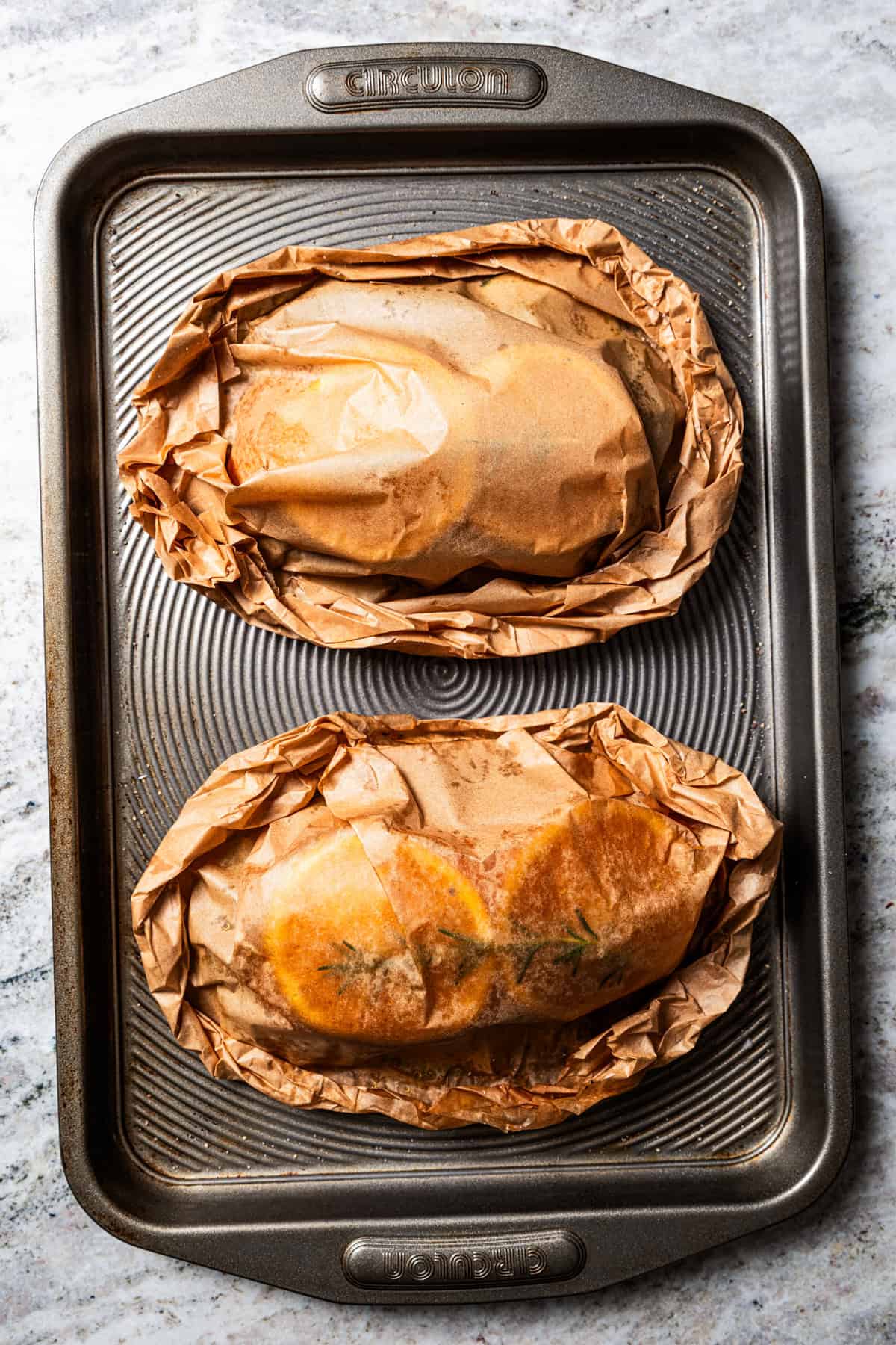 Two baked portions of salmon en papillote wrapped in parchment and placed on a baking sheet.