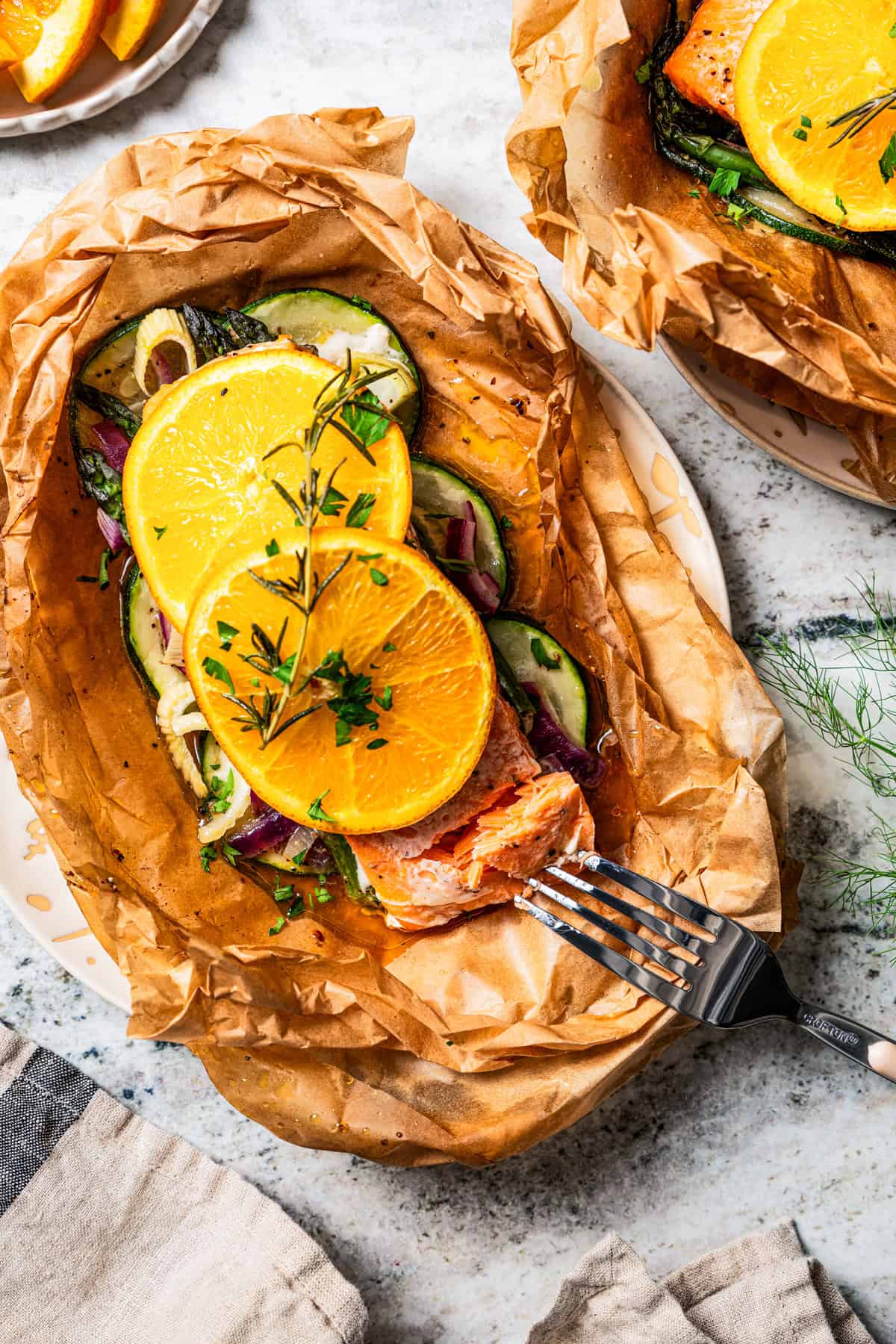 Overhead view of a fork poking into the end of a salmon filet garnished with orange slices in parchment paper.