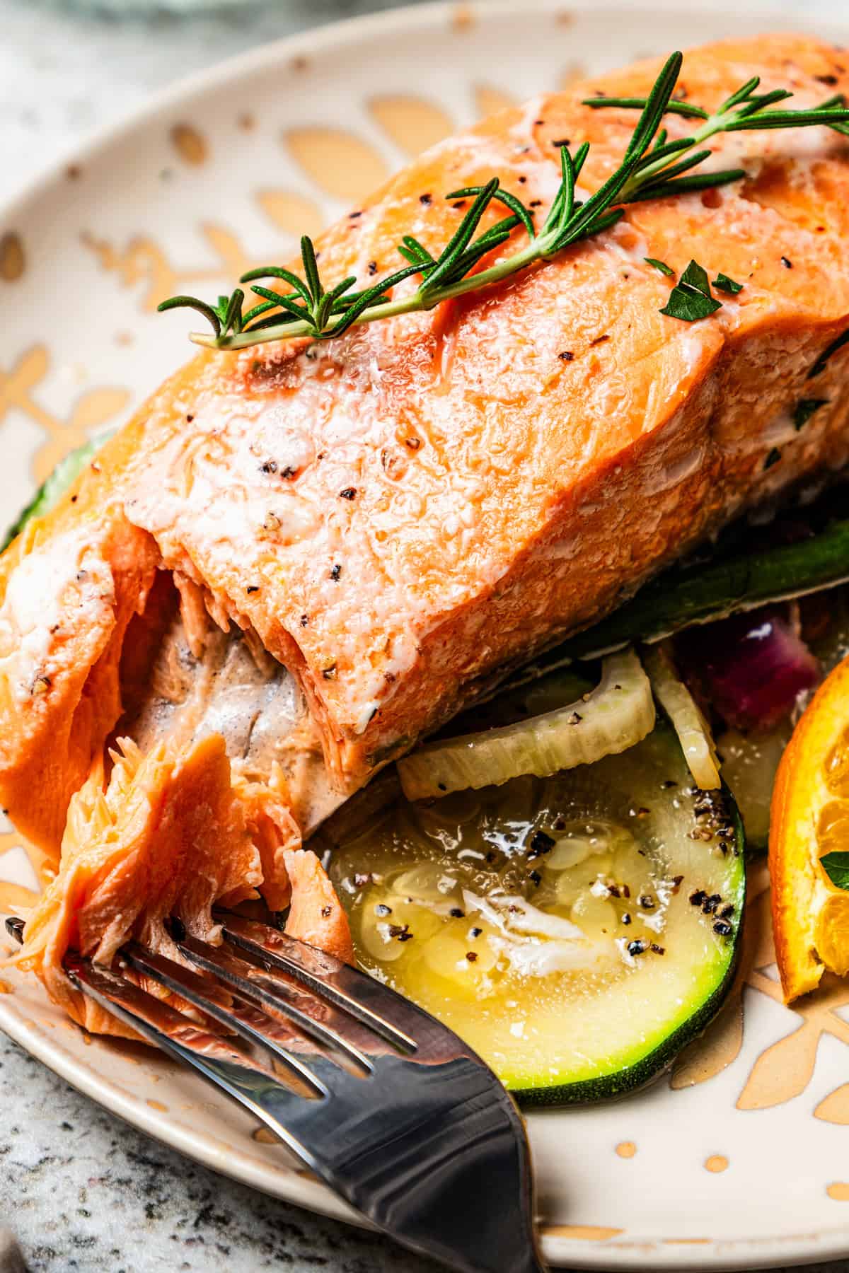 A fork flakes off a piece of salmon served on a dinner plate with sliced squash.