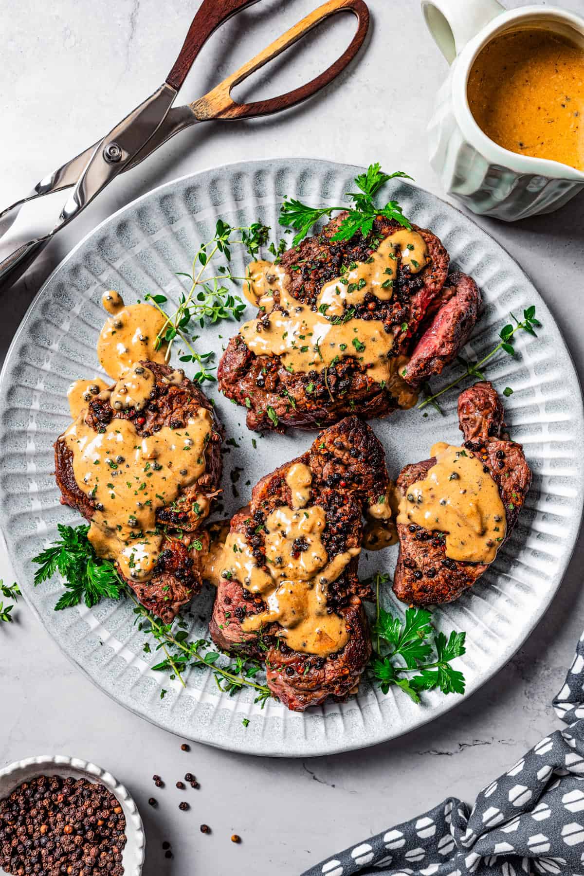 Four filet mignon steaks served on a plate and are topped with a peppercorn sauce to make steak au poivre.