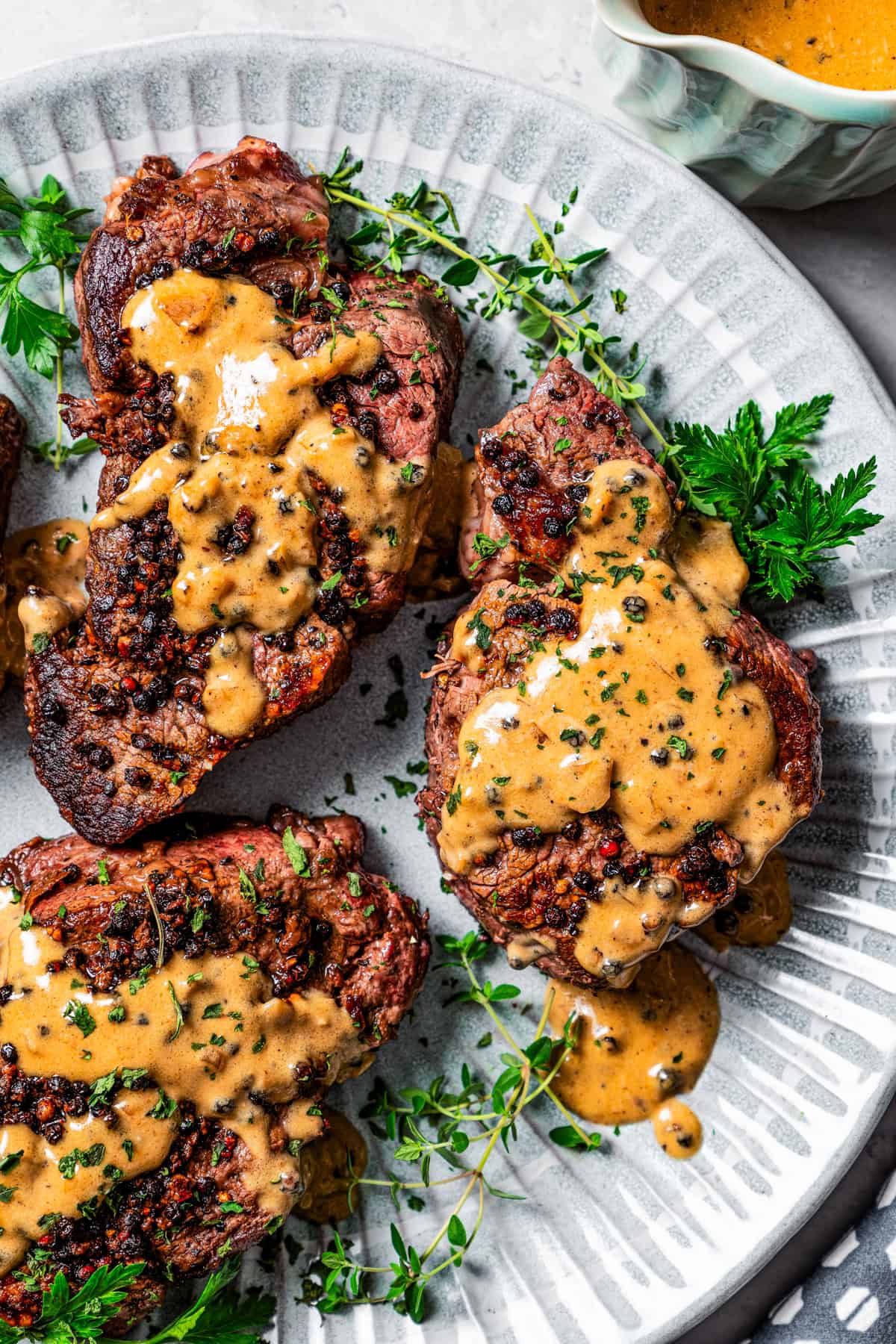 Peppercorn sauce topped steaks on a dinner plate.