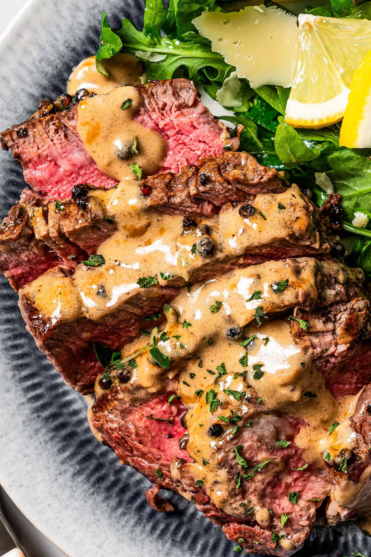 Close-up shot of a sliced steak topped with cognac sauce and peppercorns.