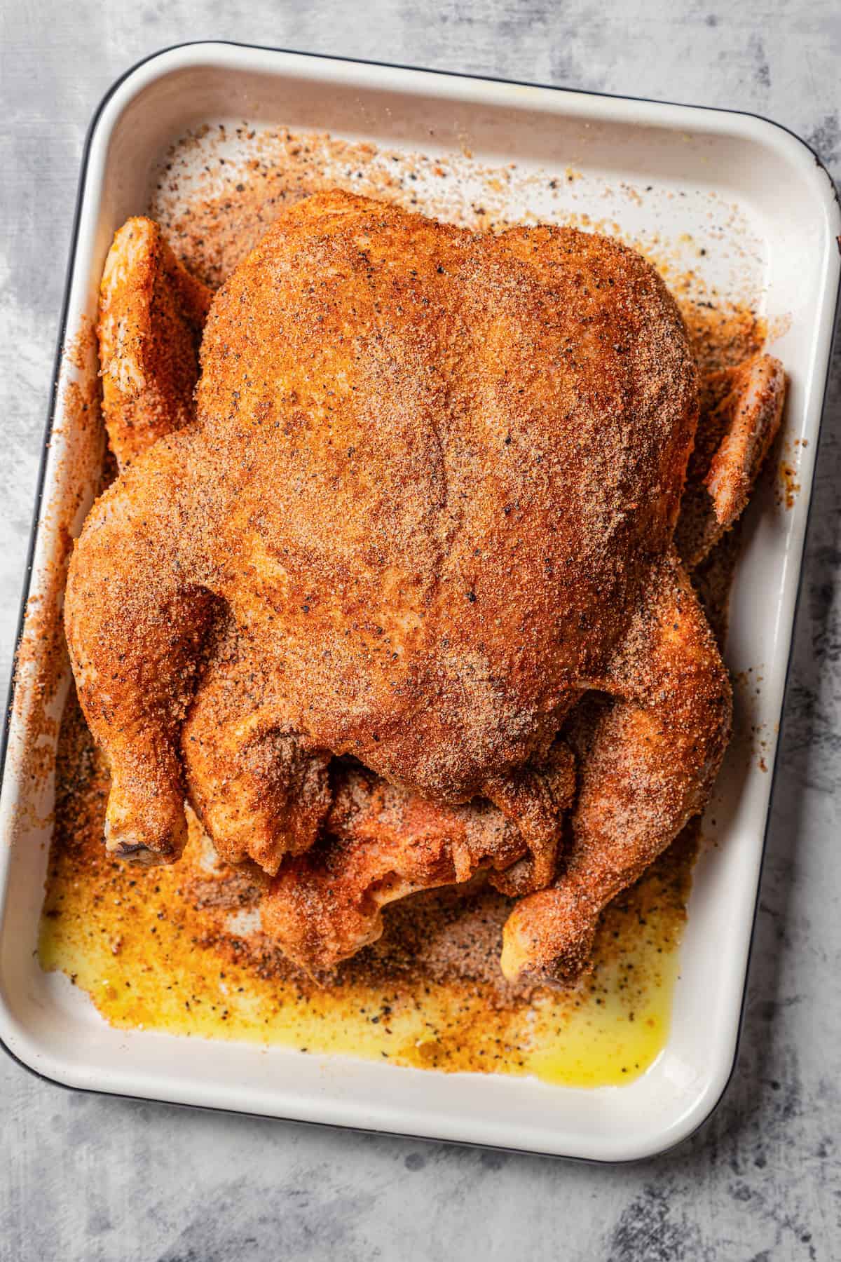 A seasoned whole chicken in a baking dish.