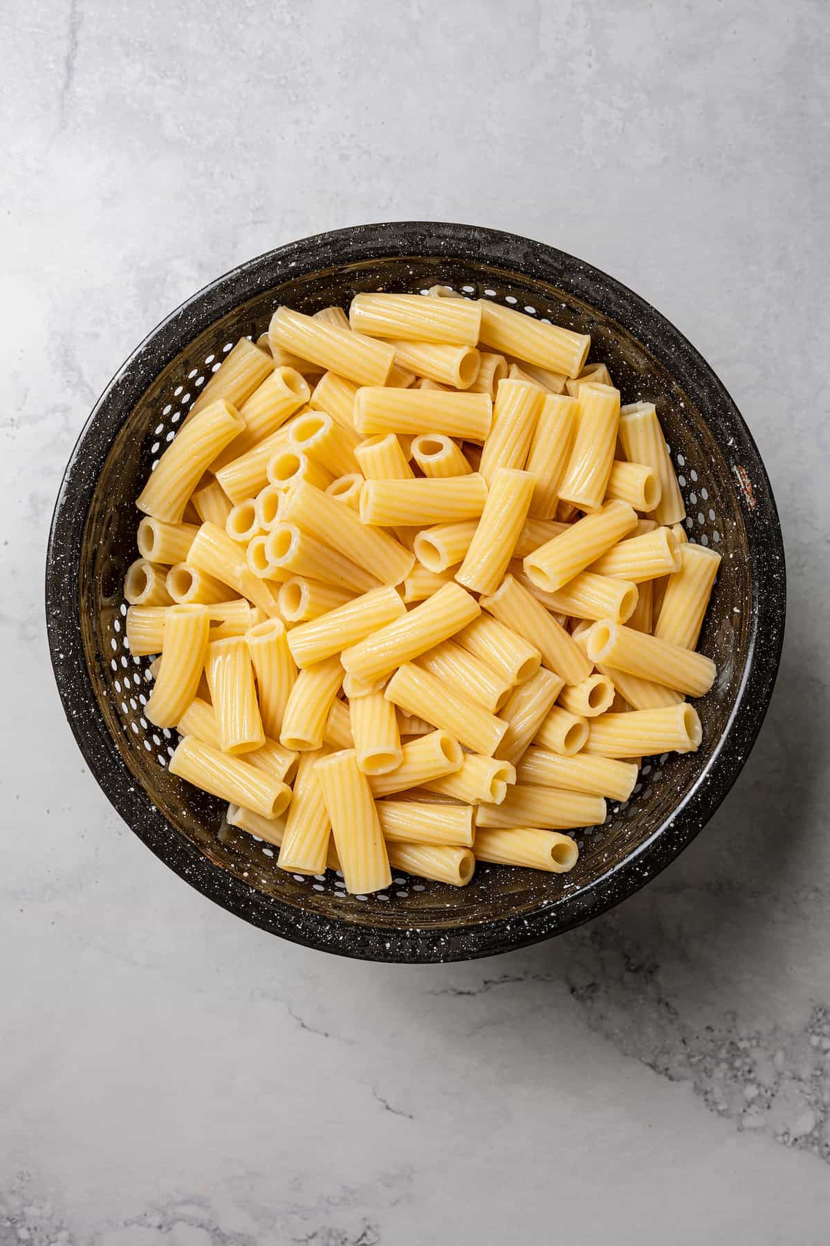 Cooked rigatoni pasta in a black colander.