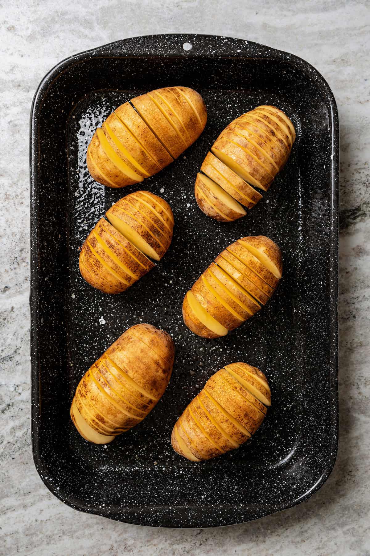 Overhead view of hasselback potatoes in a metal baking pan.