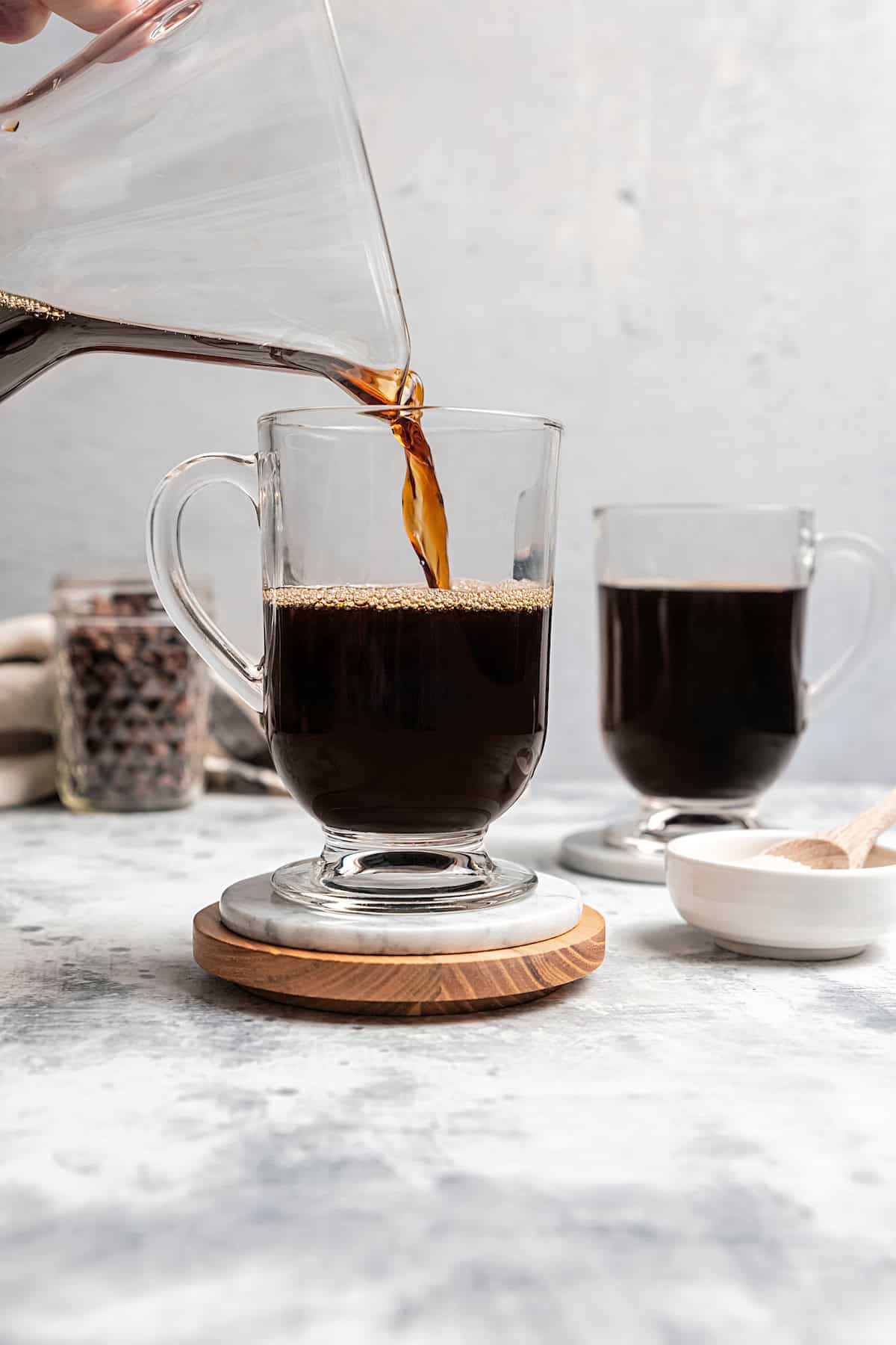 Brewed coffee being poured into a glass Irish coffee mug with a second coffee in the background.