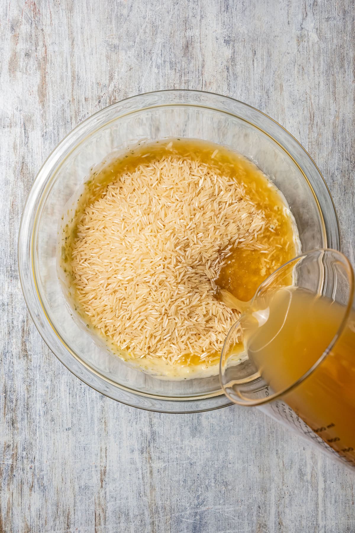 Chicken stock being added to the rice mixture in a glass bowl.