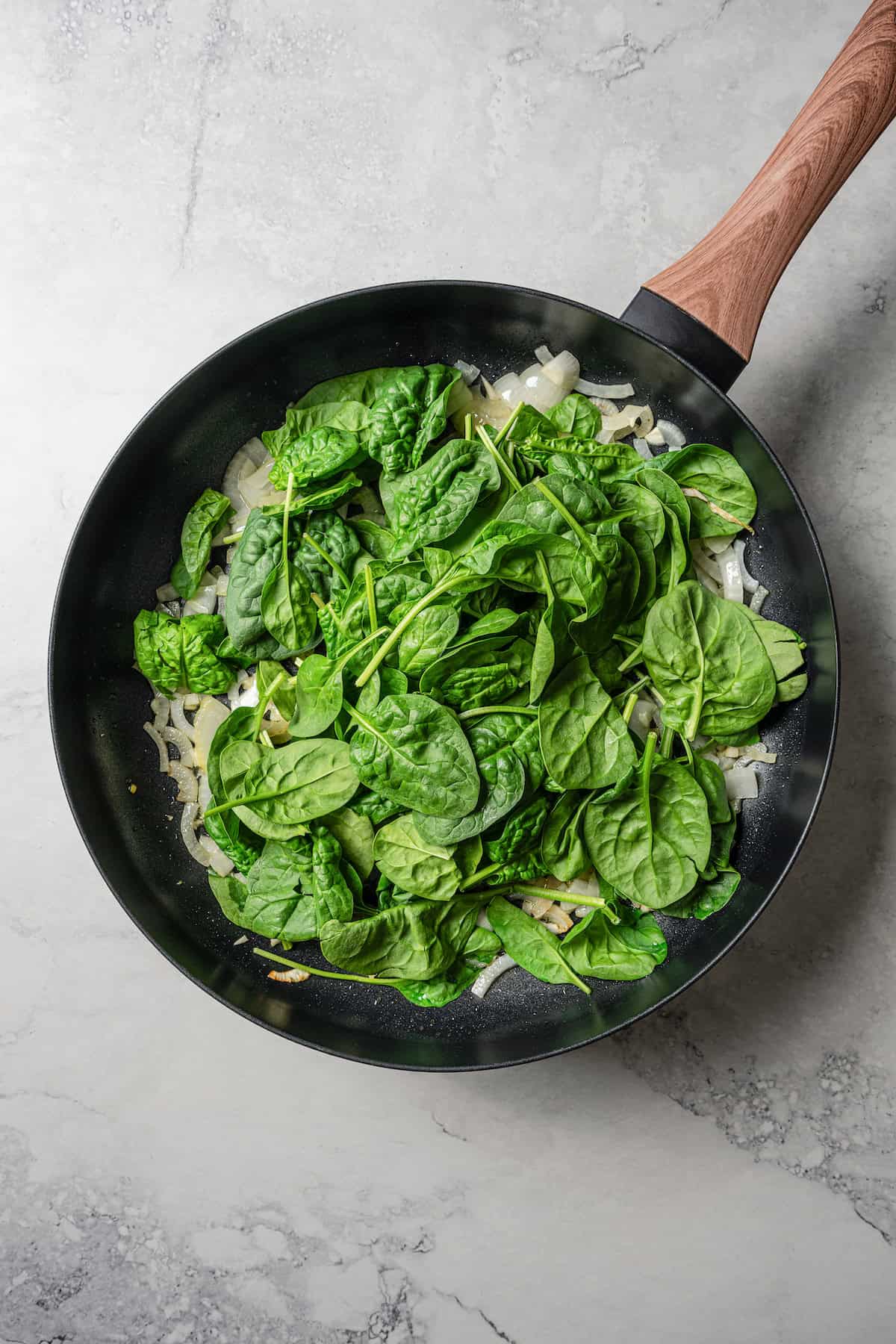 Spinach leaves added to a skillet with sautéed onions.