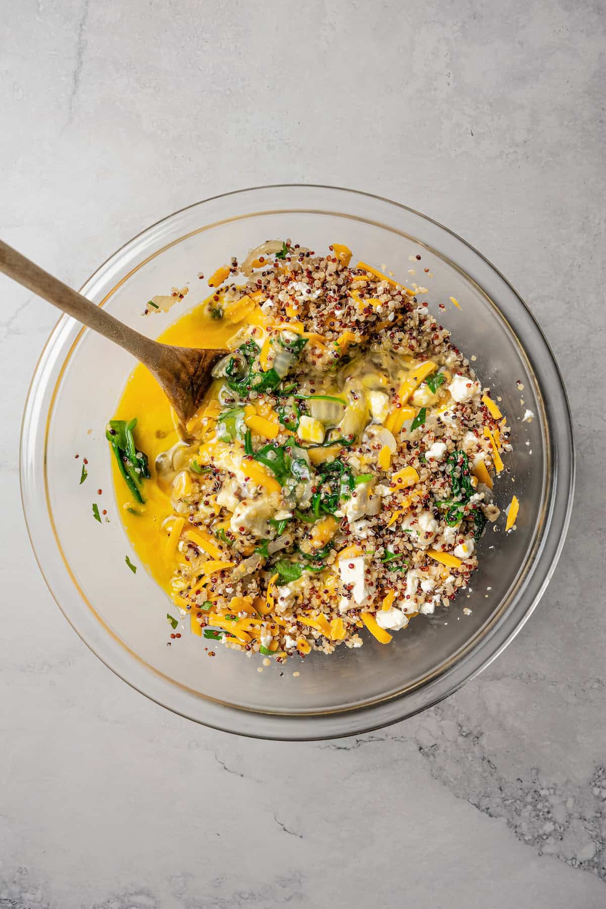 Quiche filling combined in a glass bowl with a wooden spoon.