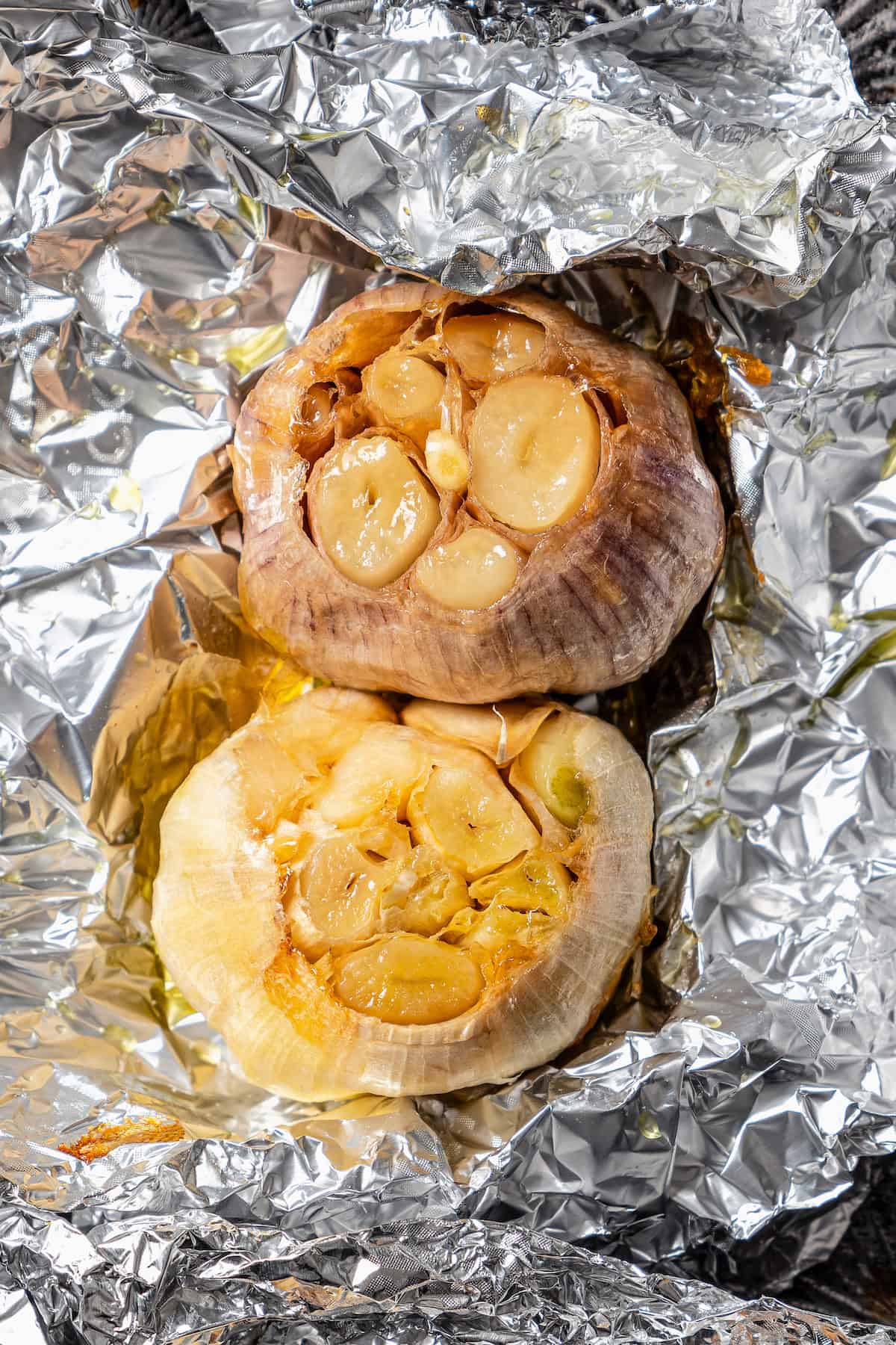 Close up of two whole roasted garlic bulbs inside foil.