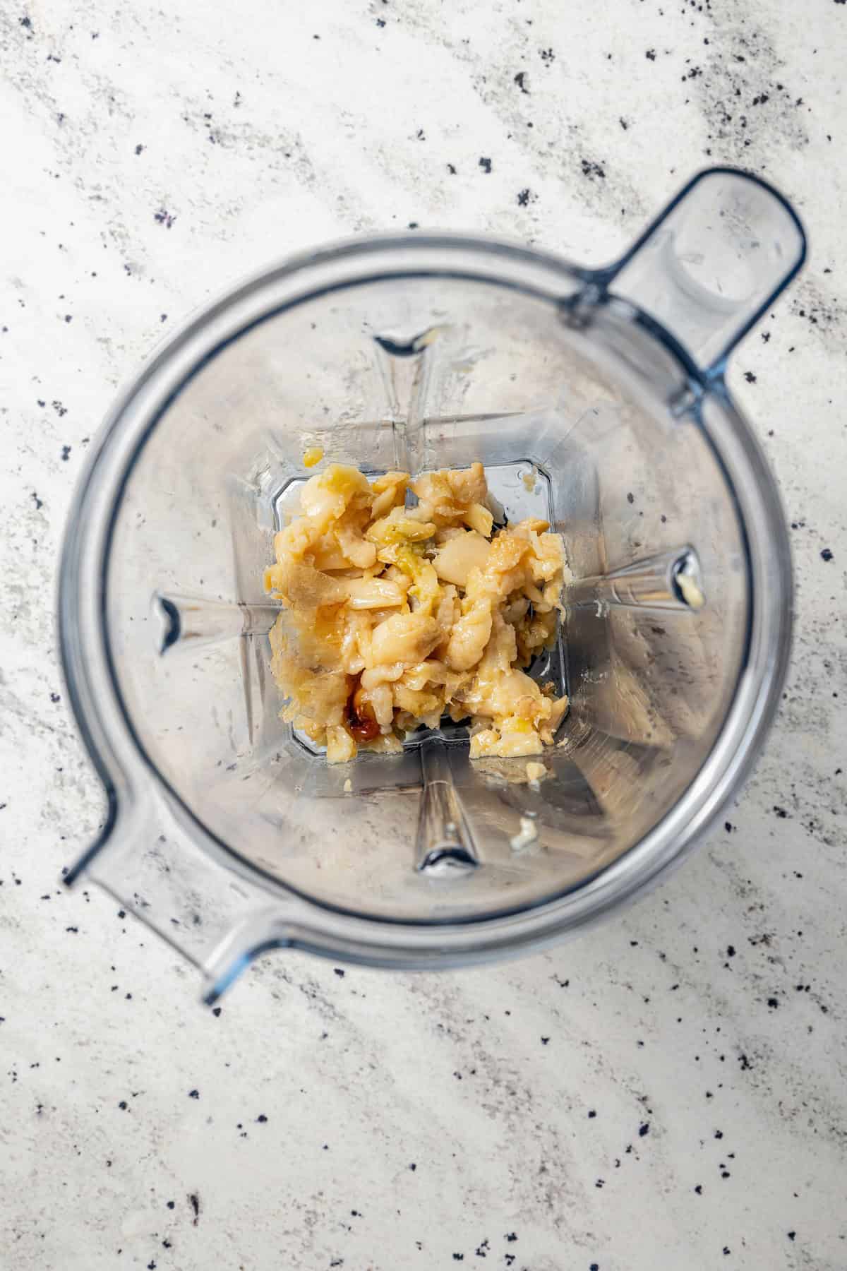 Overhead view of roasted garlic added to a blender.