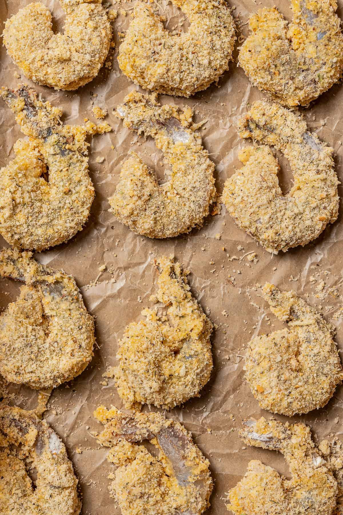 Close up of uncooked breaded shrimp on a piece of parchment paper.