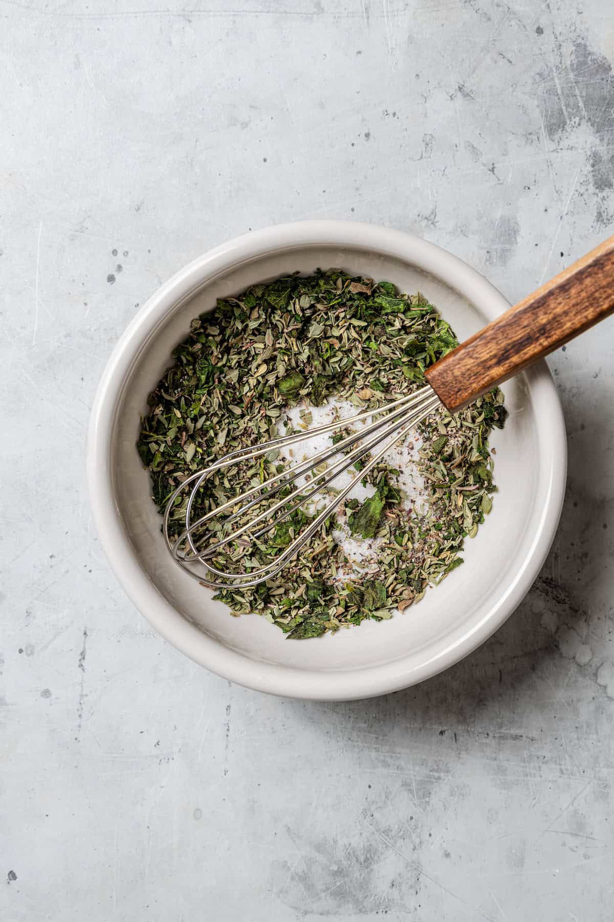 The herbs and seasoning mixture combined in a white bowl with a whisk.