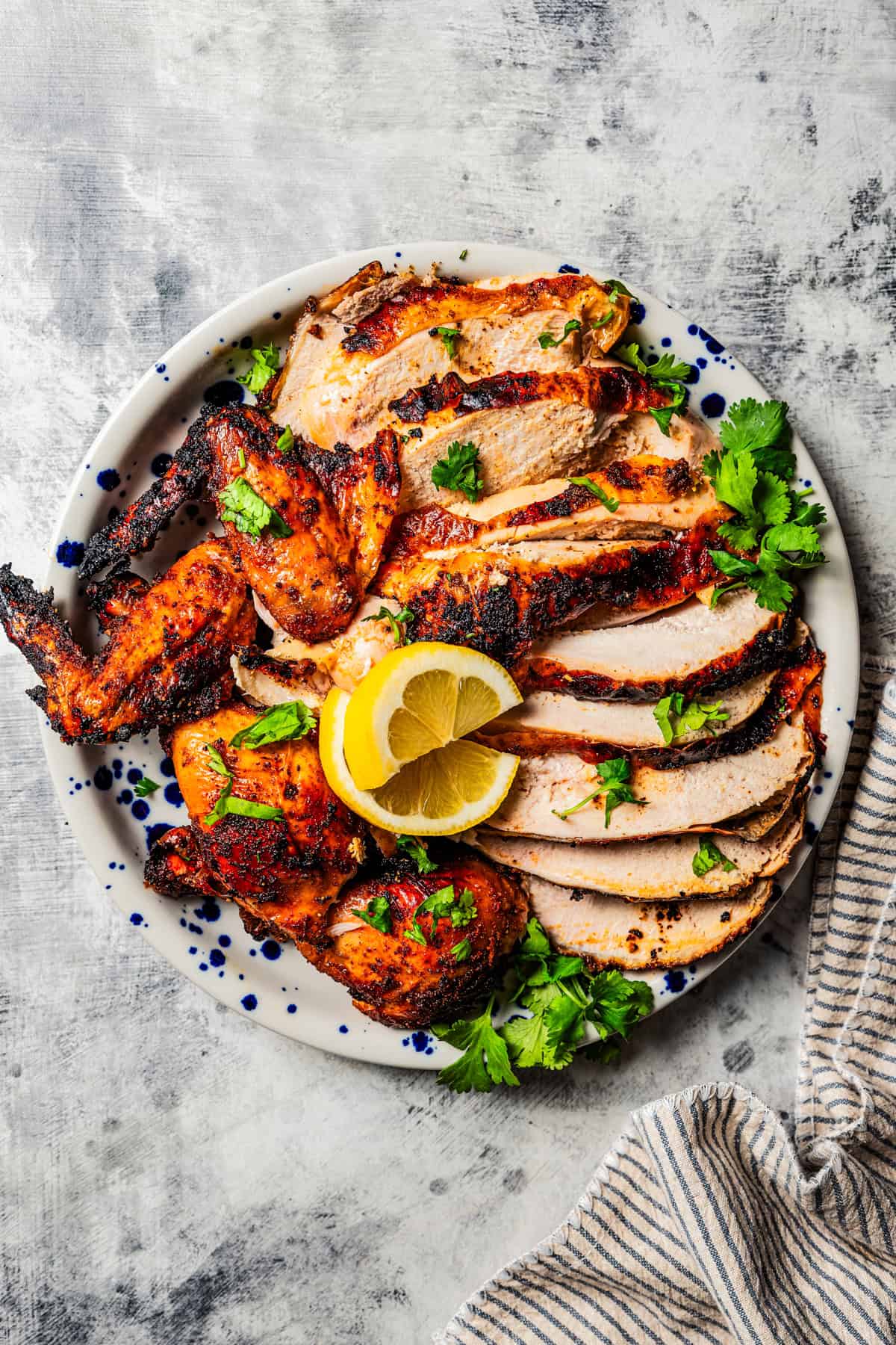 Beer can chicken sliced and served on a plate with lemons.