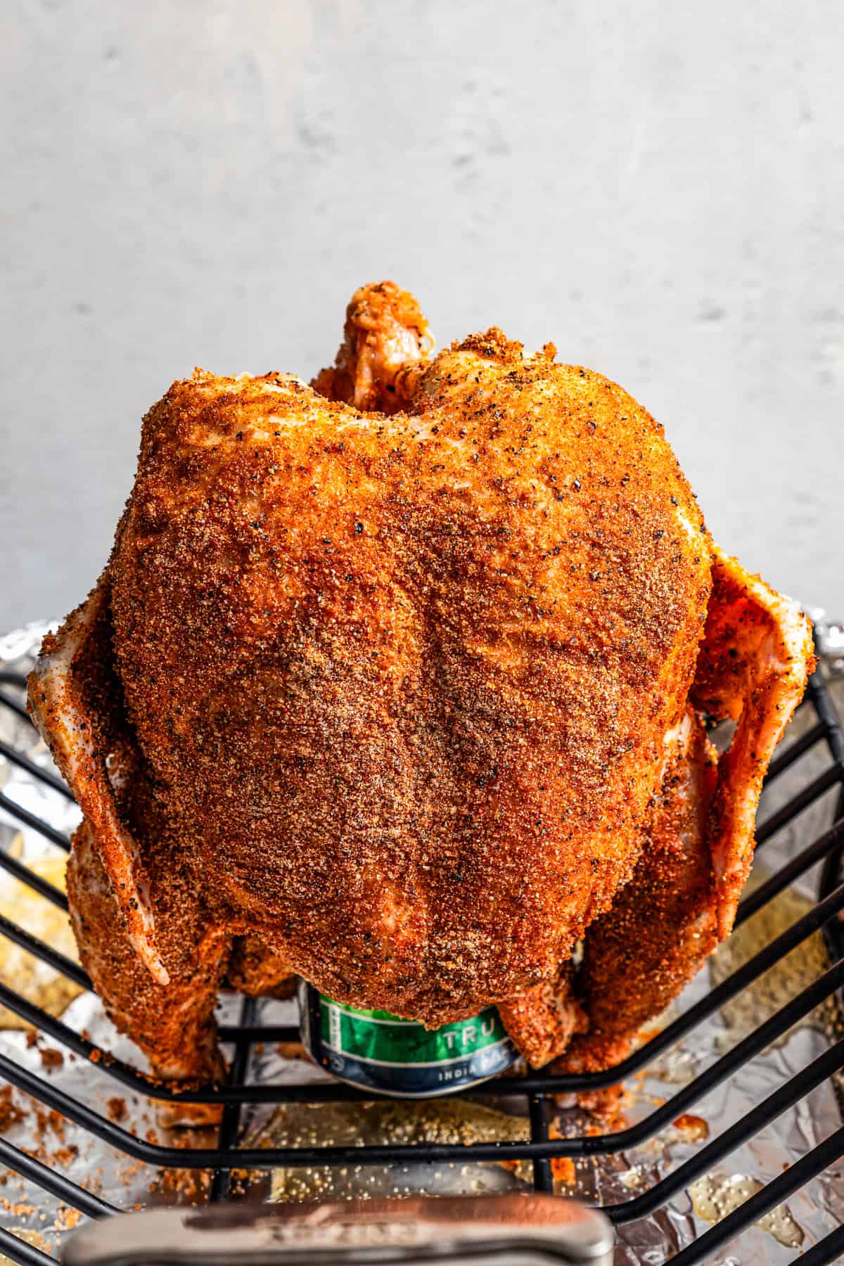 Uncooked beer can chicken propped upright over the beer can on a roasting rack.