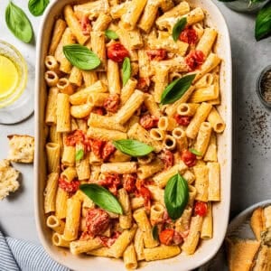 Overhead view of baked Boursin pasta in a ceramic baking dish, surrounded by pasta ingredients.