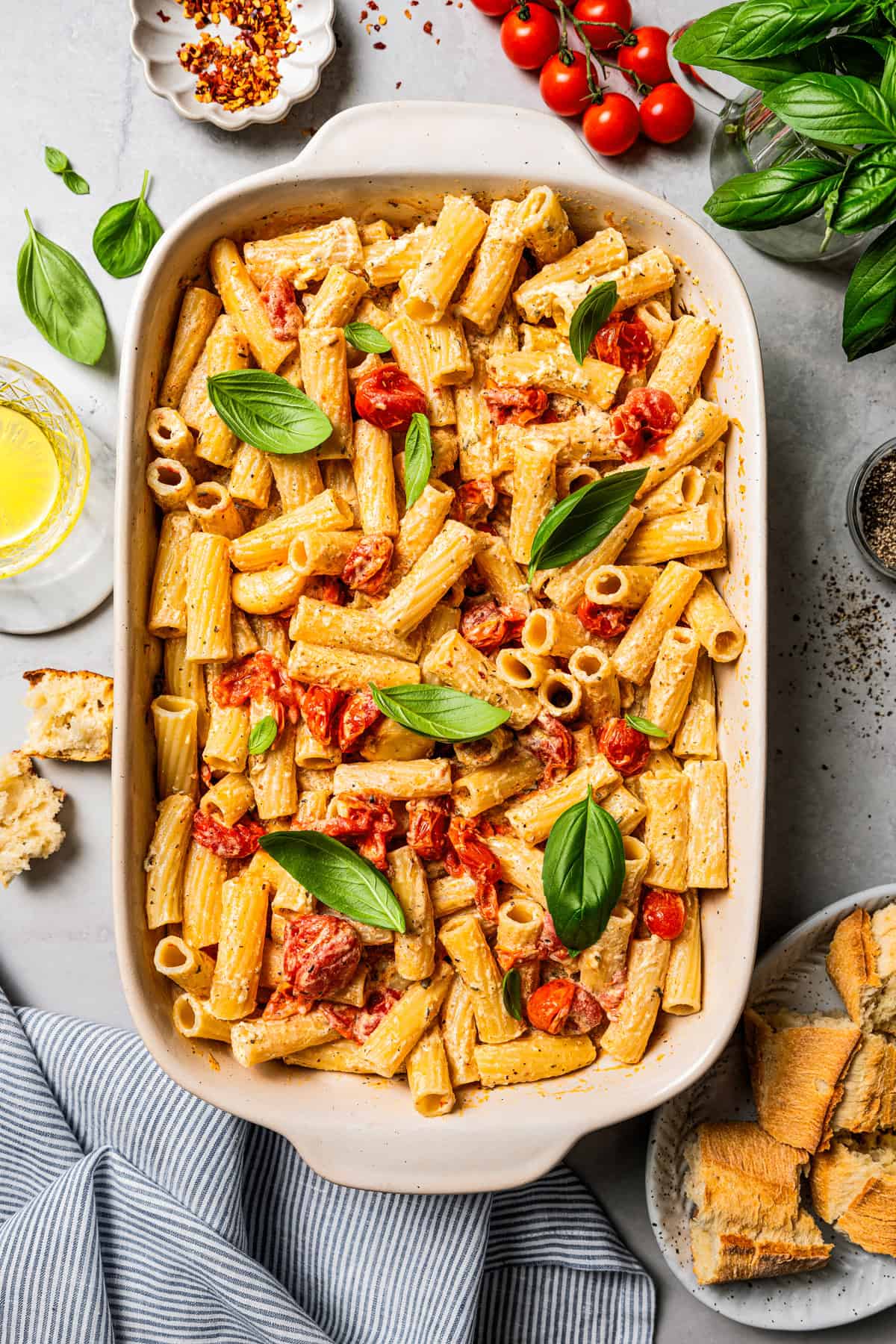 Overhead view of baked Boursin pasta in a ceramic baking dish, surrounded by pasta ingredients.