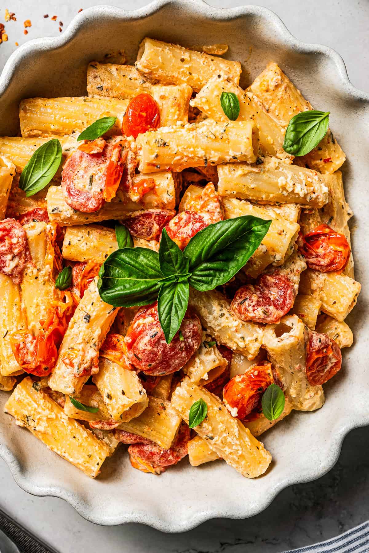 Pasta rigatoni mixed with tomatoes and cheese and served in a bowl with a garnish of fresh basil leaves.