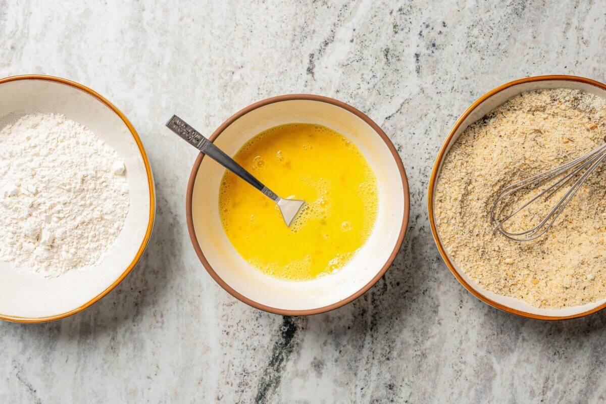 Shrimp parmigiana is crispy breaded shrimp baked over tangy marinara sauce with a golden, cheesy mozzarella crust. Perfect served with pasta! Breading station with bowls of breadcrumbs, flour, and egg.