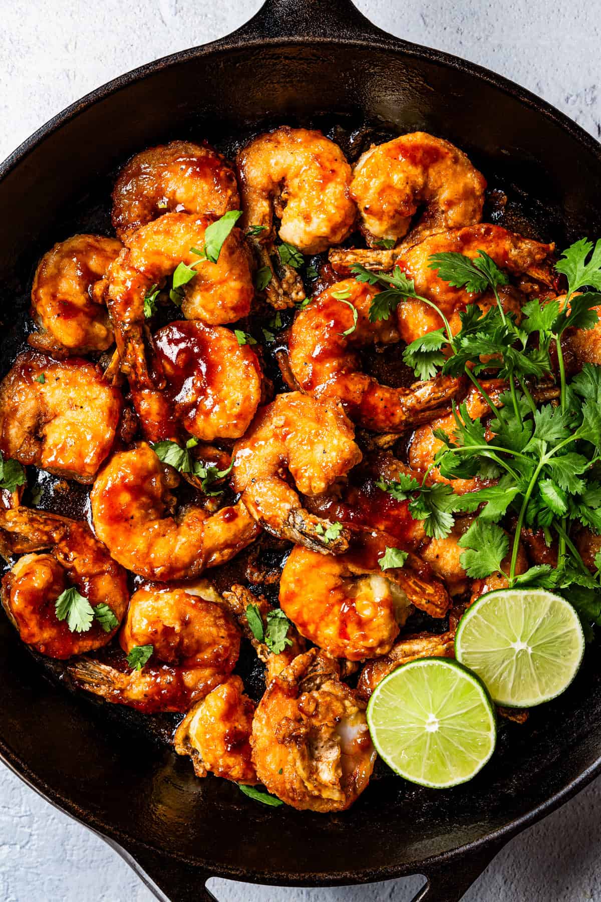 Firecracker shrimp in a skillet garnished with cilantro and lime leaves.