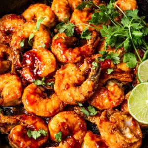 Cooked shrimp in a skillet garnished with cilantro and lime leaves.