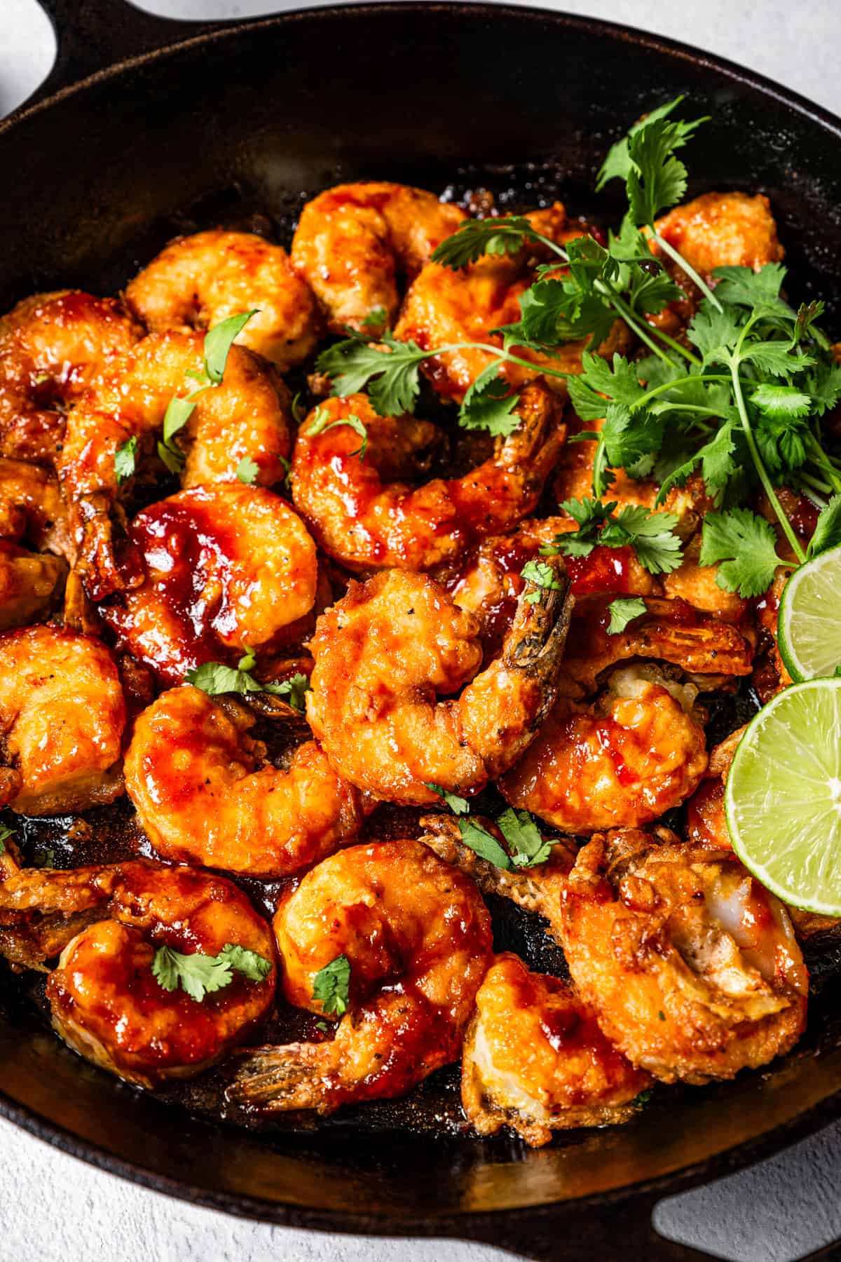 Cooked shrimp in a skillet garnished with cilantro and lime leaves.