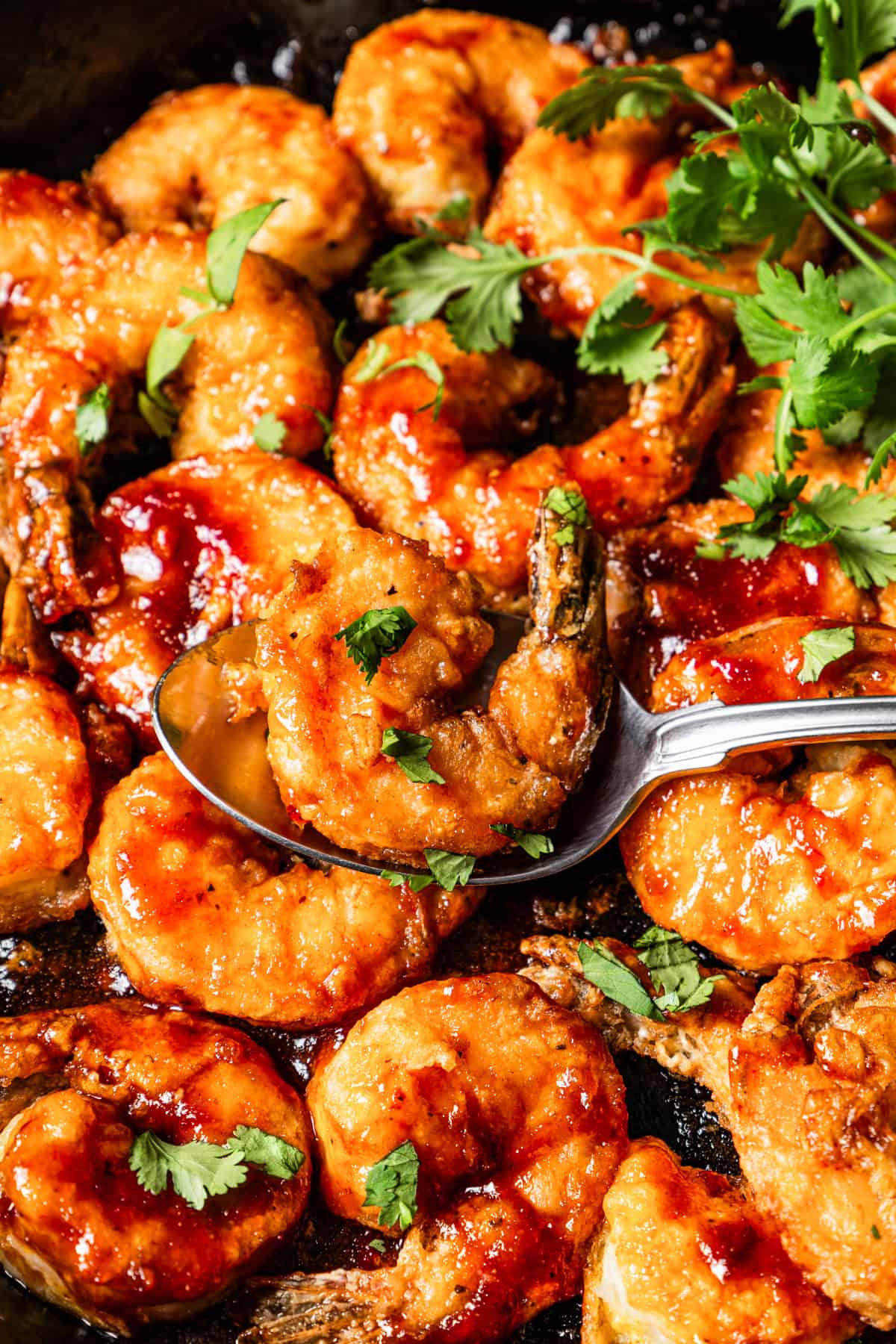 Close-up of a spoon scooping firecracker shrimp from a skillet.