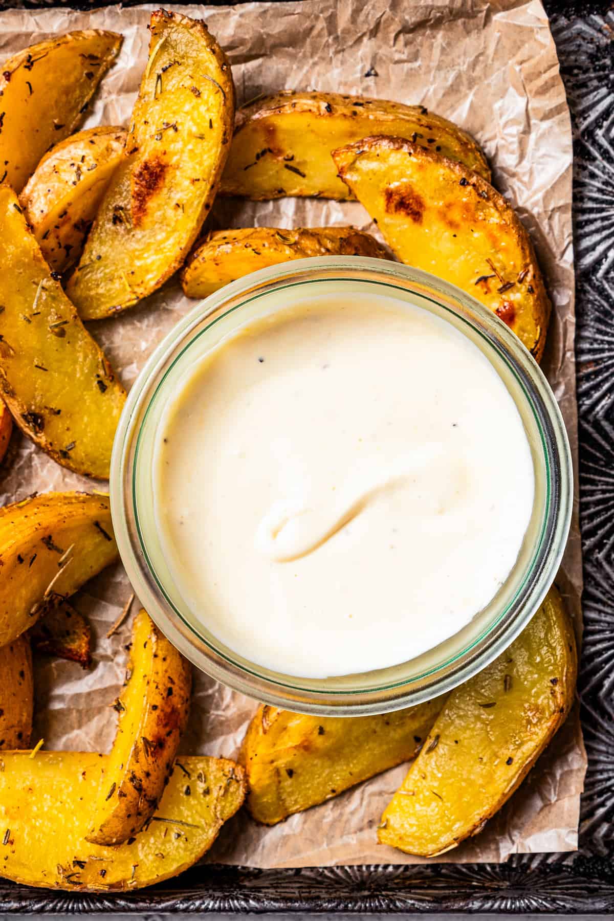 A small bowl of garlic aioli surrounded by potato wedges on a tray.