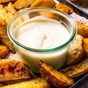 A small bowl of roasted garlic aioli surrounded by potato wedges on a tray.