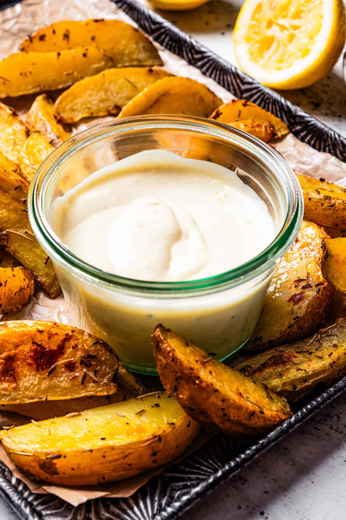 A small bowl of roasted garlic aioli surrounded by potato wedges on a tray.