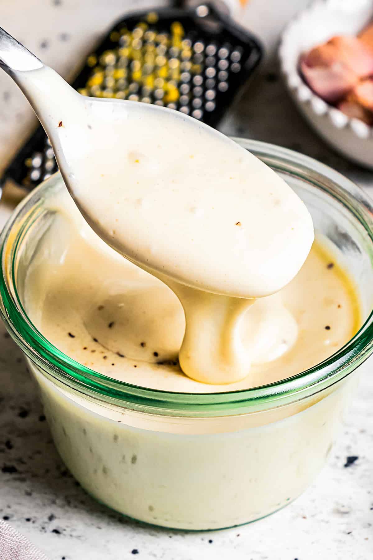 A spoon scooping aioli from a small glass bowl, with a lemon and citrus zester in the background.