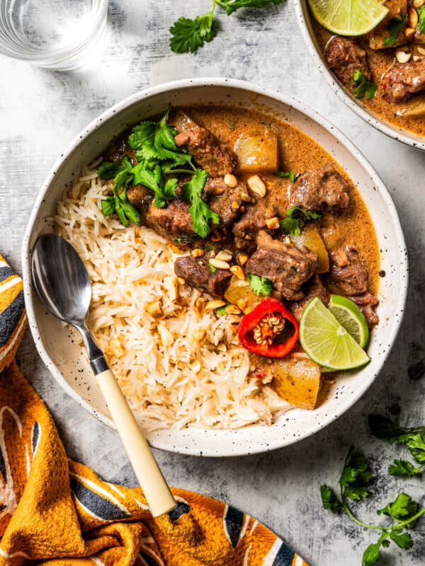 Curry served in bowls with rice, with fresh herbs and a striped dishcloth placed near the bowls.