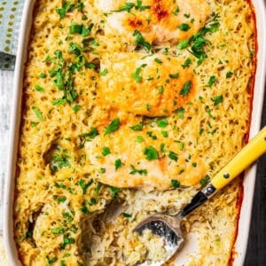 Overhead view of a baked no peek chicken and rice casserole garnished with chopped parsley, with a serving spoon resting in the space where a chicken breast was served.