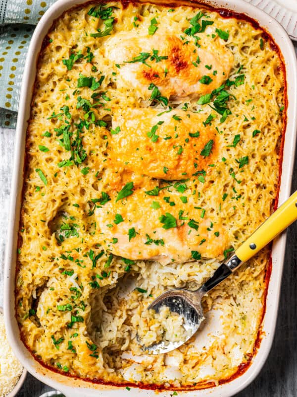 Overhead view of a baked no peek chicken and rice casserole garnished with chopped parsley, with a serving spoon resting in the space where a chicken breast was served.