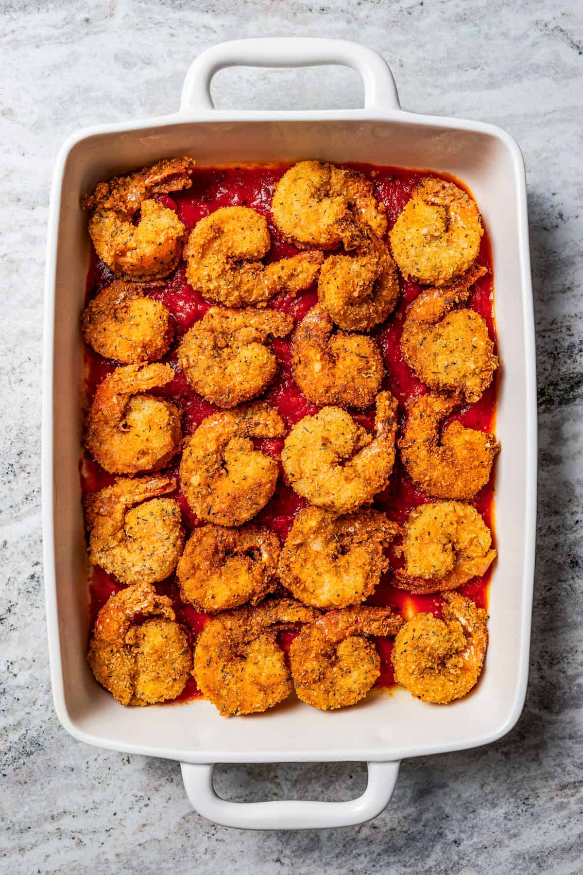 Shrimp layered over marinara in a baking dish.